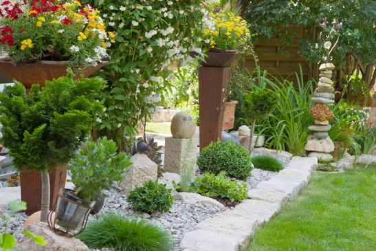 Jardin paysager extérieur avec aménagement décoratif comprenant massifs fleuris surélevés, bordures en pierre naturelle, paillis minéral gris, arbustes taillés en boule, graminées ornementales