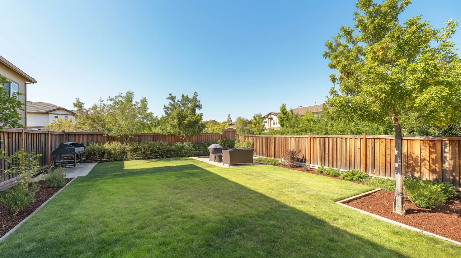 Jardin résidentiel avec pelouse verdoyante entretenue, clôture en bois naturel, aménagement paysager avec paillis brun et plantations périphériques