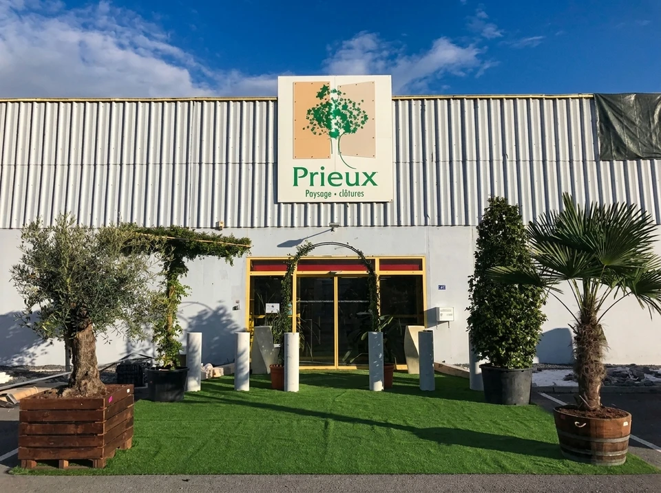 Photographie intérieure d'un showroom spacieux et lumineux dédié aux aménagements extérieurs, présentant des maquettes de jardins, des échantillons de matériaux (bois, composite, carrelage minéral), des clôtures exposées, des modèles de pergolas bioclimatiques, et des équipements de piscine. L'espace doit être accueillant, bien rangé, avec une signalisation claire, et si possible montrer quelques clients ou un conseiller interagissant avec les produits exposés. L'atmosphère doit être professionnelle et inspirer la confiance.